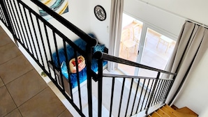 Eine Treppe mit schwarzer Geländer, ein Bild an der Wand, ein Deckenlüfter und Blick auf eine Außenpatio mit Stühlen.