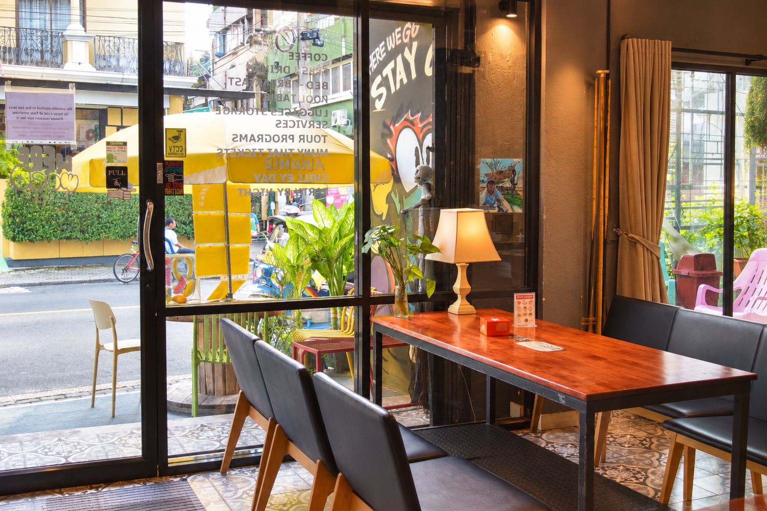 A hotel room with a wooden table, chairs, a lamp, and a view of the street outside.