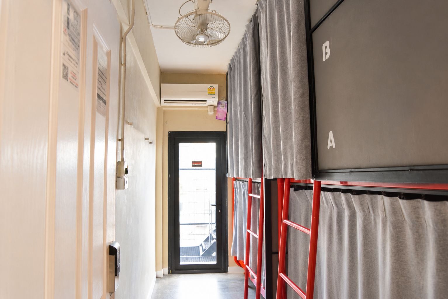 Un pasillo con un ventilador de techo, una puerta con un letrero y una pared con la letra 'B'.