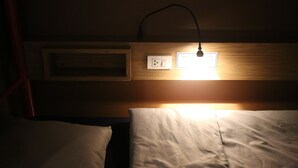 Een hotelkamer in gedimd licht met een enkel bed, een nachtkastje en een wandlamp.