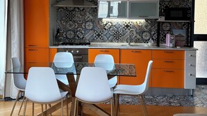 Una cocina moderna con gabinetes naranjas, una mesa de comedor blanca con sillas y una alfombra gris.
