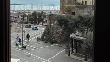Une vue d’un bâtiment historique doté d’une tour, d’un port de plaisance avec des bateaux et d’une rue où l’on peut voir des piétons et des véhicules.