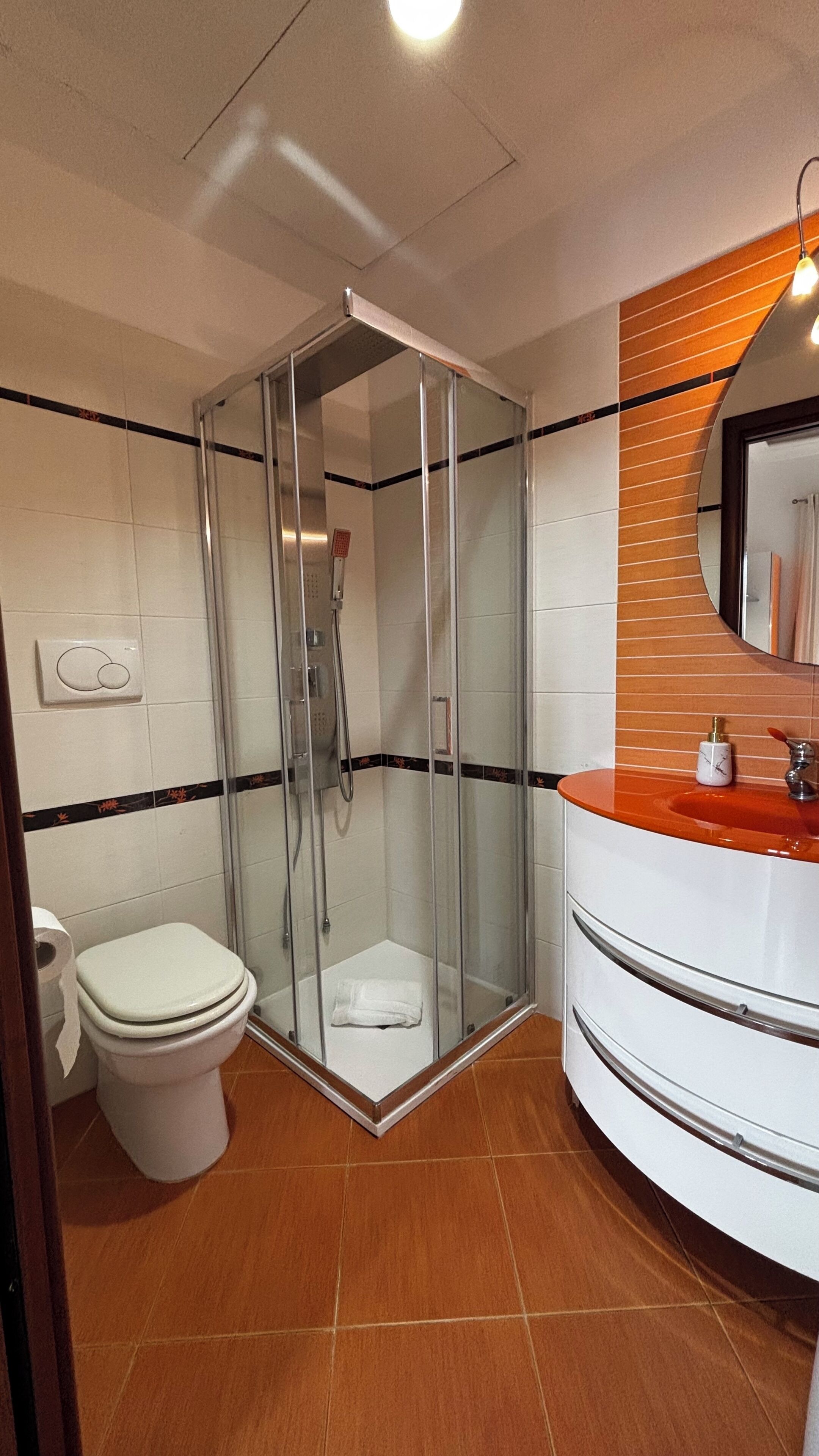 A bathroom with a glass-enclosed shower, a white toilet, and a curved sink with a mirror above it.