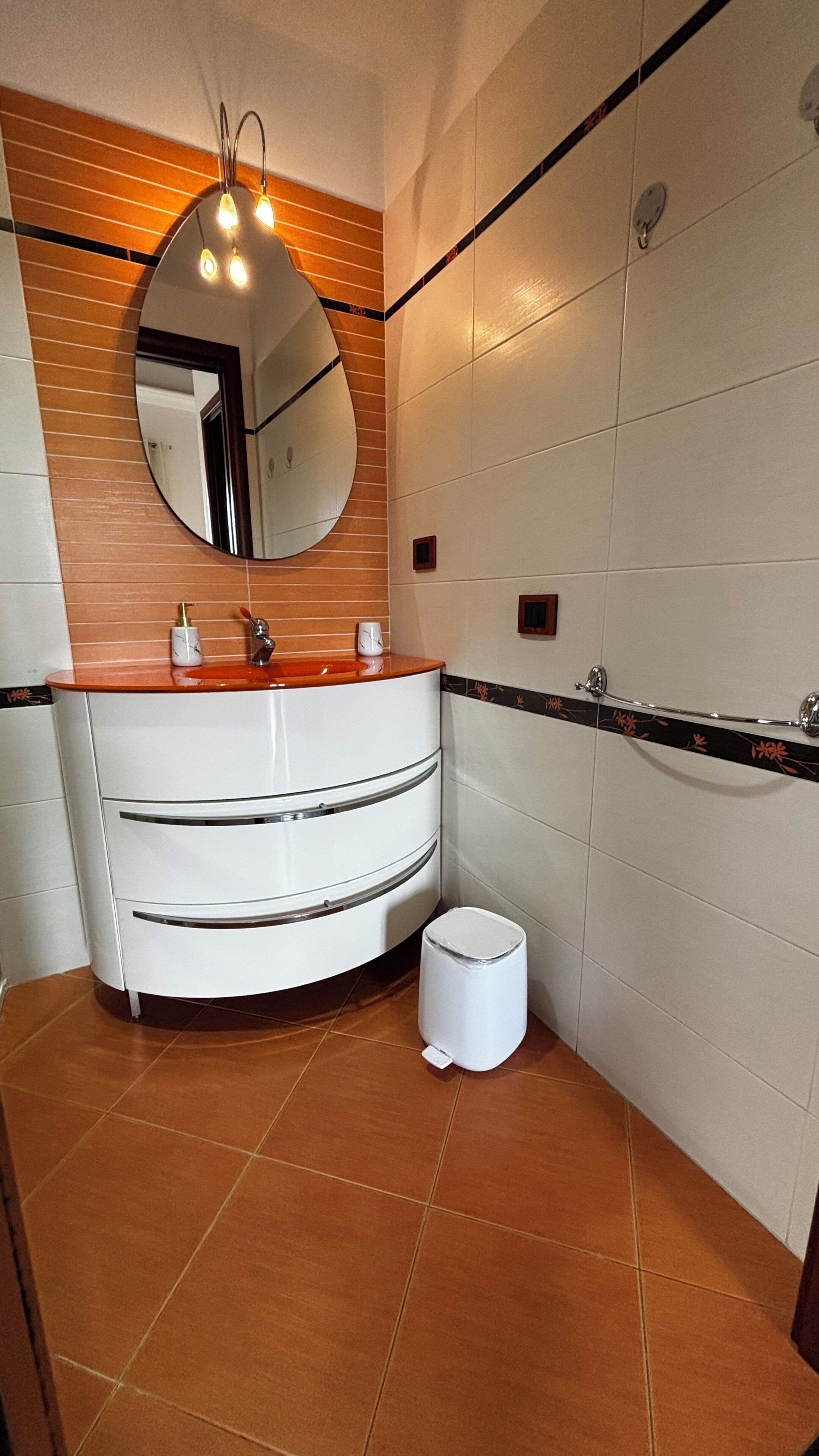 A bathroom with a white vanity, a round mirror, a towel rack, and a toilet.