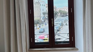 Una habitación con un ventanal grande, suelo de madera y vistas a una calle con edificios y coches.