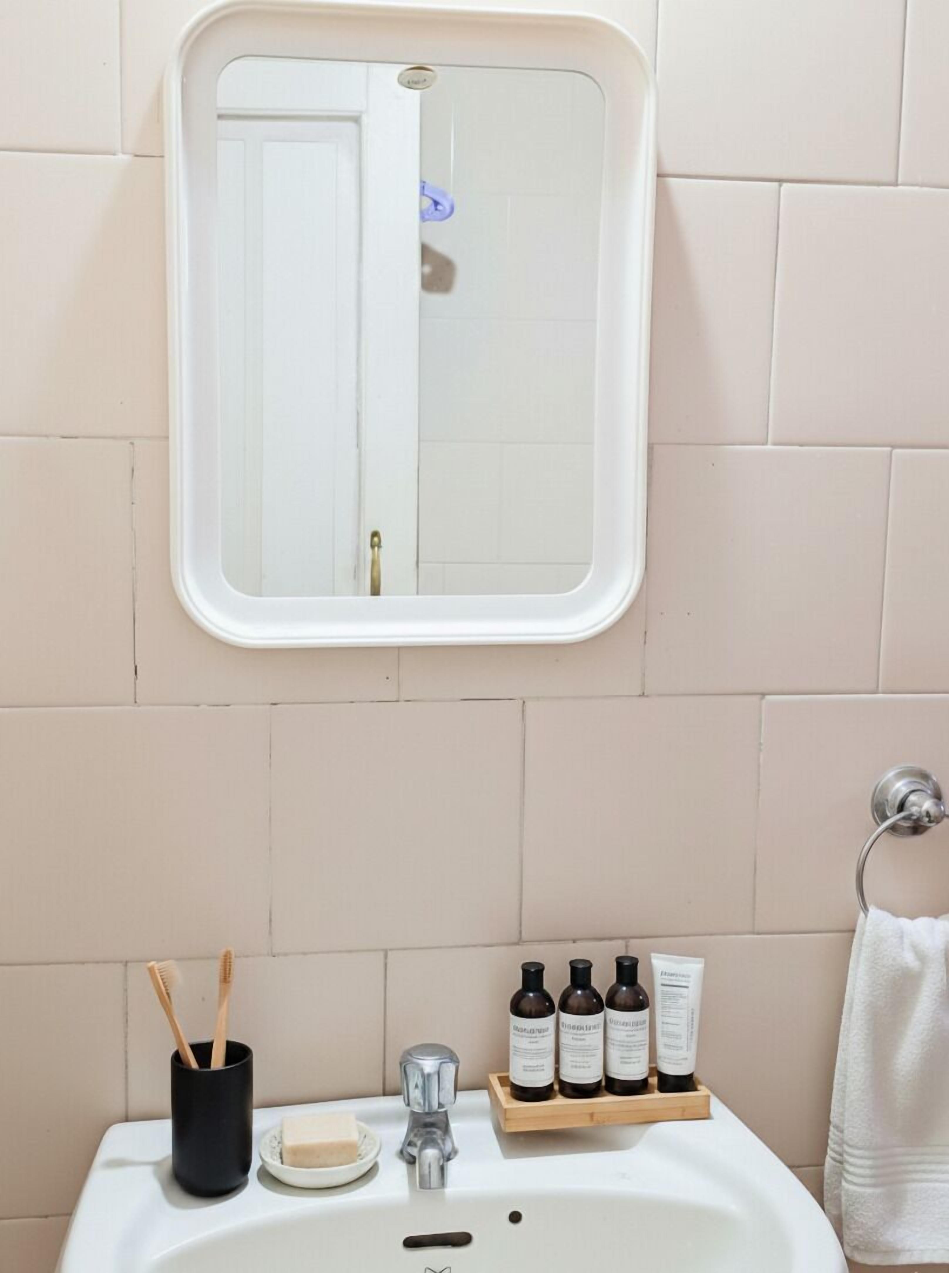 Un baño con un lavamanos blanco, un espejo, un porta cepillos de dientes y un jabonera.