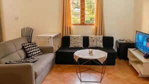 Una sala de estar con un sofá, una mesita redonda, un televisor y una ventana con cortinas.