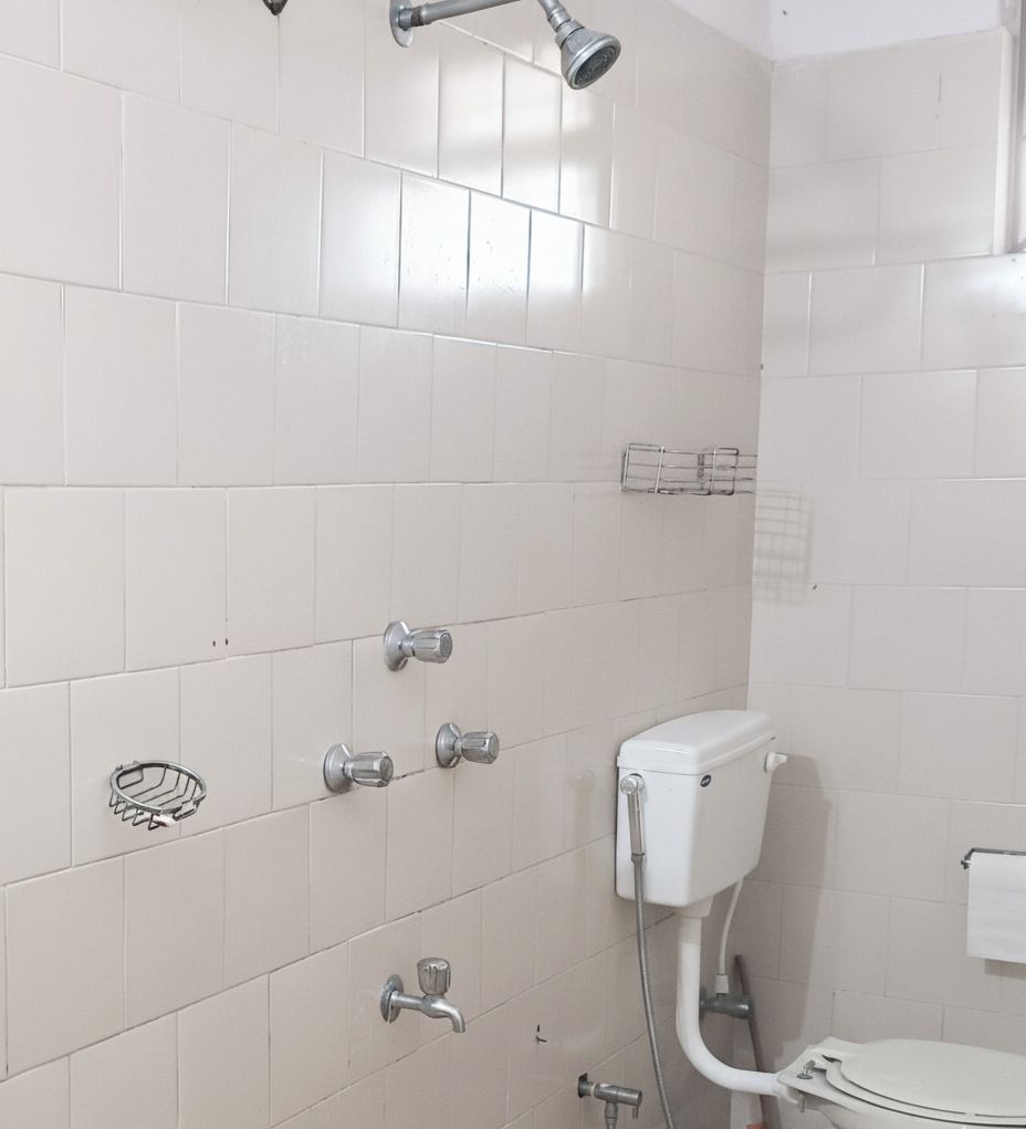 Une salle de bain avec des murs carrelés de carreaux blancs, des toilettes, une douche avec un pommeau de douche amovible et un porte-serviettes.