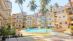 Un hotel de varios pisos con balcones, piscina y palmeras.