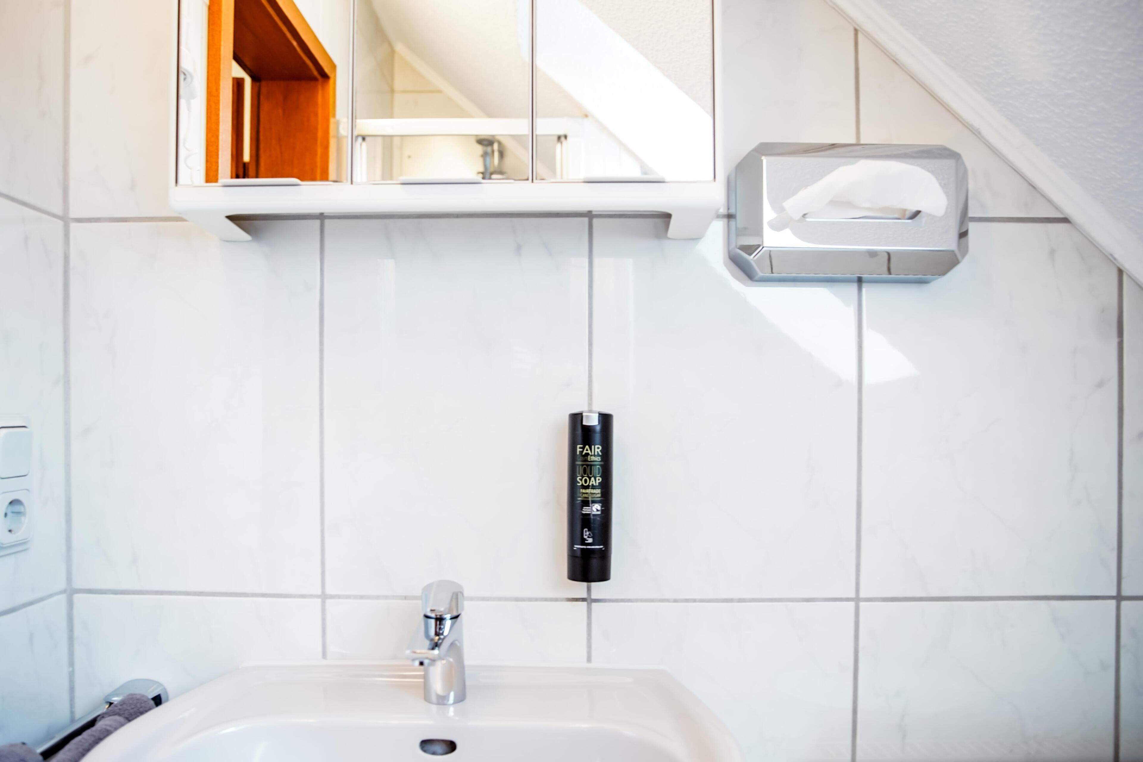 A bathroom with a white sink, a mirror, and a soap dispenser on the wall.