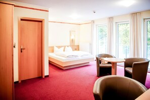 Ett hotellrum med en säng, ett skrivbord, två stolar och ett fönster med gardiner.