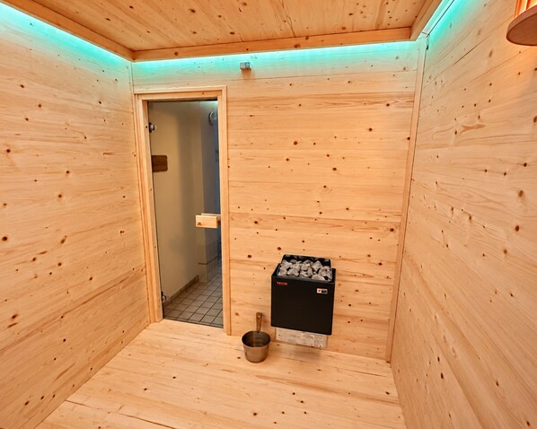 A sauna room with wooden walls, a door, a bench, and a heater.