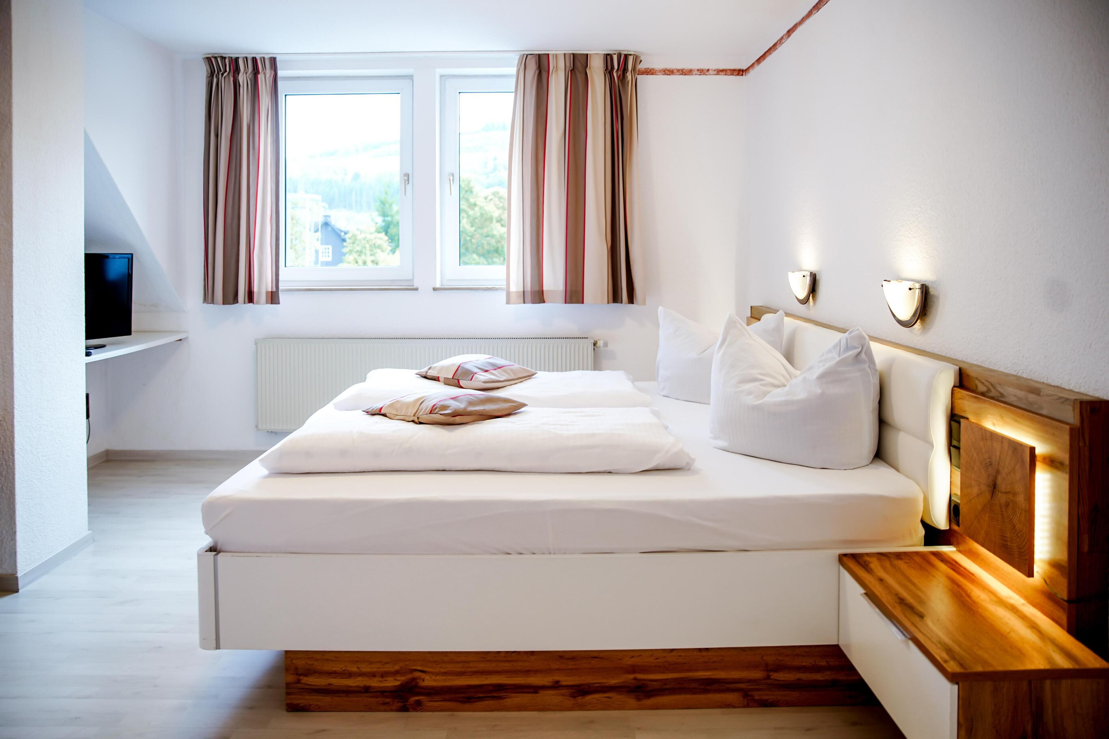 A bedroom with a bed, bedside tables, a TV, and a window with curtains.