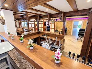 A hotel lobby with a wooden reception desk, potted orchids, a coffee machine, and a seating area with a view of the outside. - A comfortable and versatile room—perfect for relaxation, work, and socializing (Winterberg)