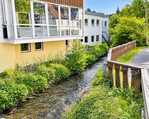 Un bâtiment moderne à la façade jaune, avec un petit ruisseau qui le longe et un pont en bois.