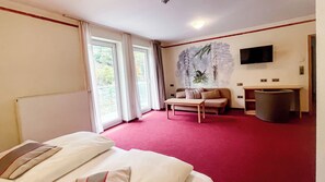 Une chambre d’hôtel comprenant un lit, un canapé, une petite table, un téléviseur fixé au mur et une fenêtre avec des rideaux.