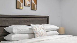 A neatly made bed with white bedding and a patterned pillow, a wooden headboard, and a lamp on a bedside table. - Perfect 2BR Airdrie Suite - Near Calgary, WiFi (Airdrie)