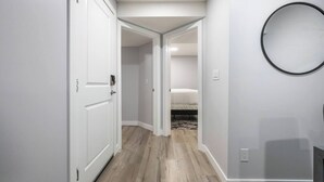 A hallway with white walls, a wooden floor, and a bed in the adjacent room. - Perfect 2BR Airdrie Suite - Near Calgary, WiFi (Airdrie)