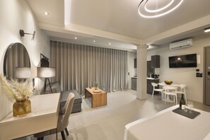 A modern living room with a dining area, a kitchen, and a TV mounted on the wall.