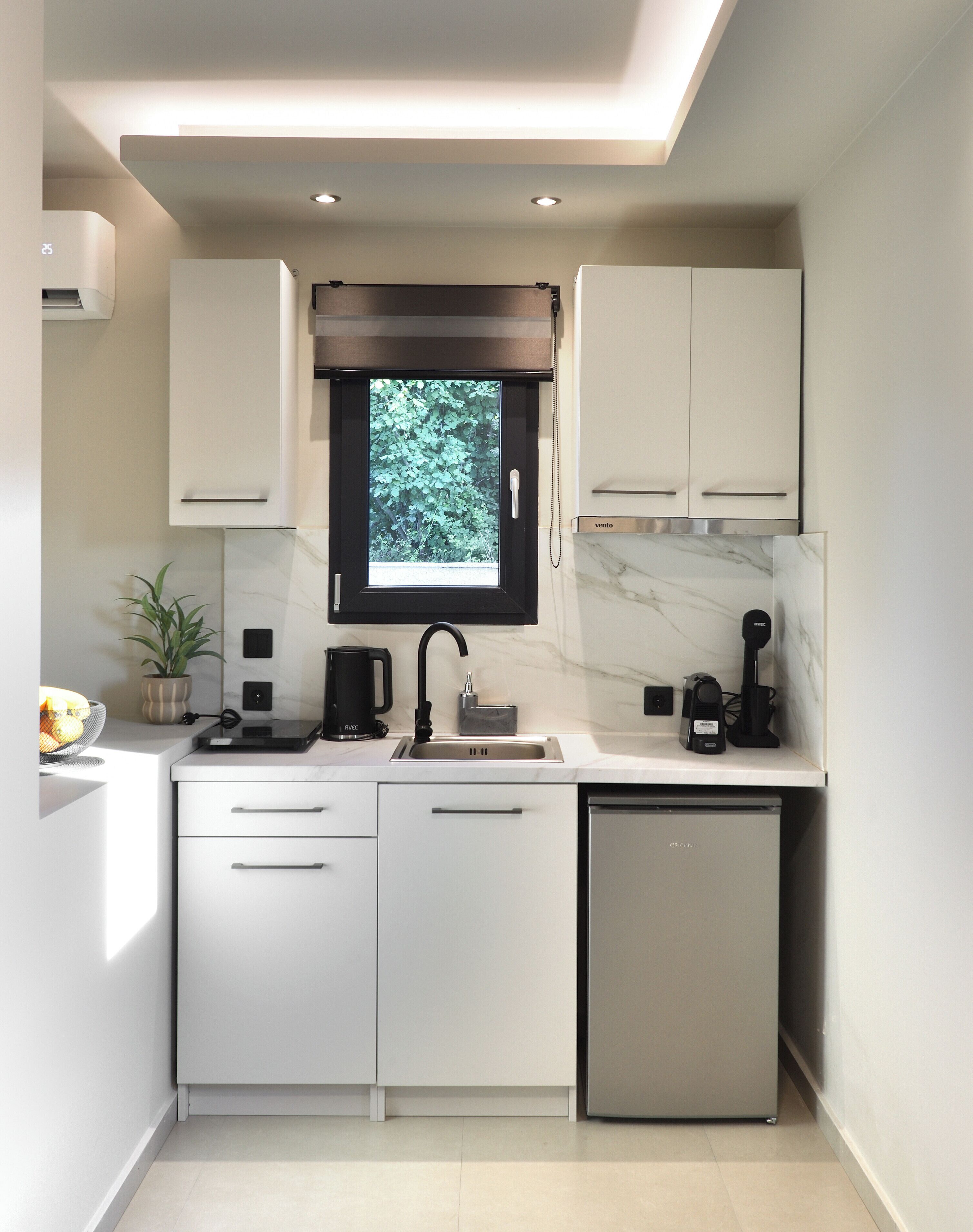 A modern kitchen with white cabinetry, a built-in window, a sink, and a compact refrigerator.