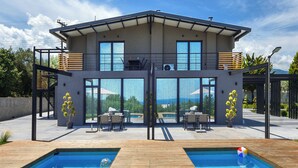 Une maison moderne dotée d’une grande façade vitrée, d’une piscine et de mobilier d’extérieur.
