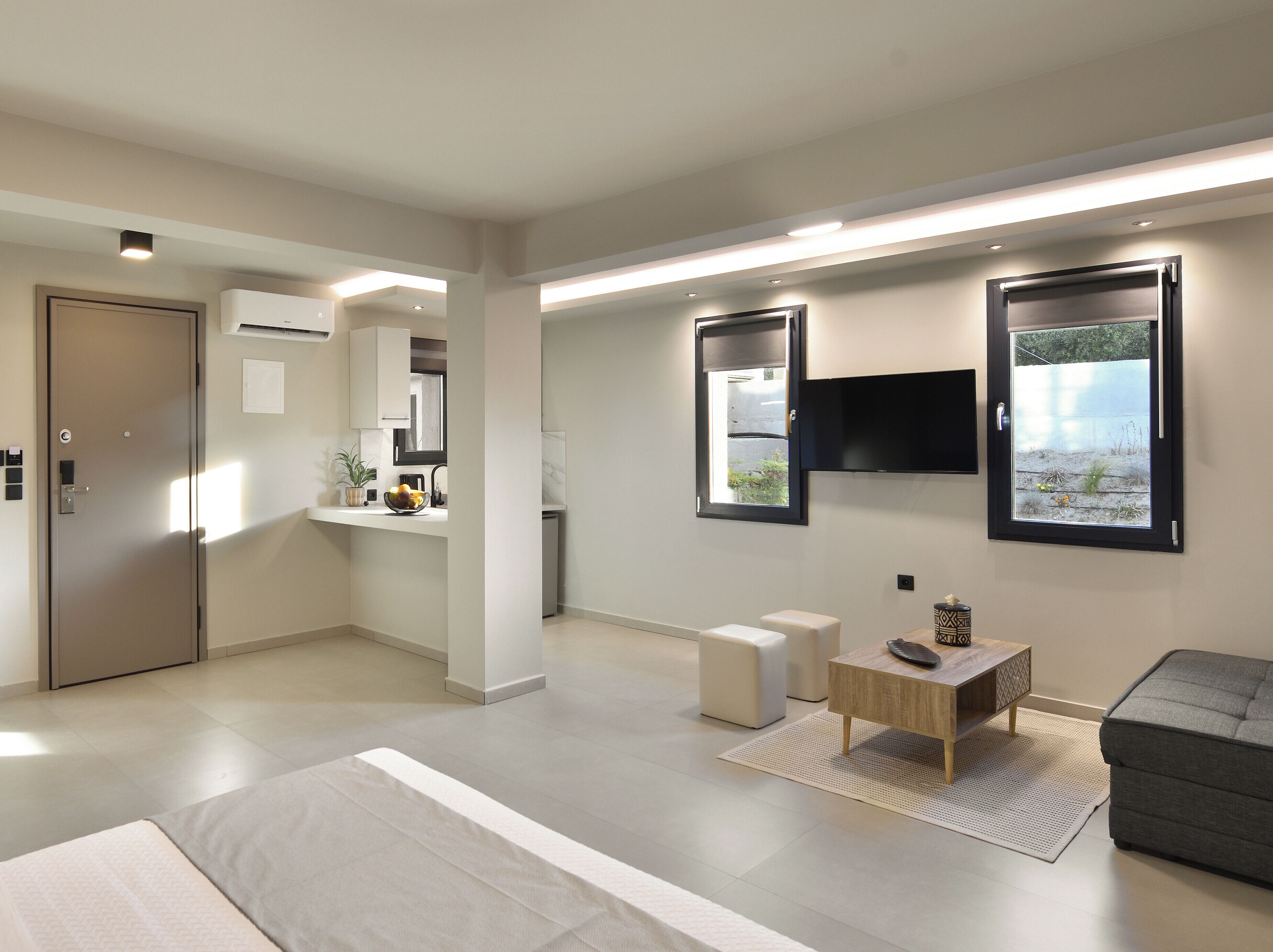 Una habitación moderna y bien iluminada con una cama, un pequeño rincón de descanso, un televisor montado en la pared y una ventana con vistas al exterior.