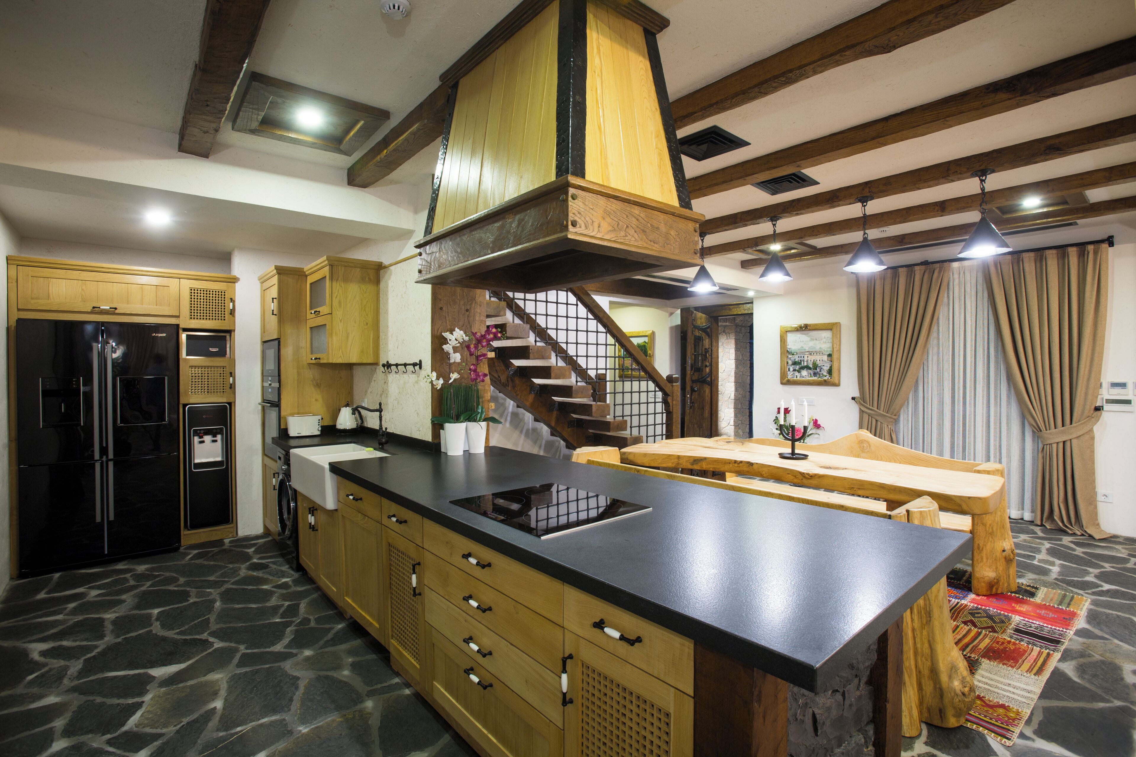 A kitchen with a stone floor, wooden cabinets, a black countertop, and a built-in stove.