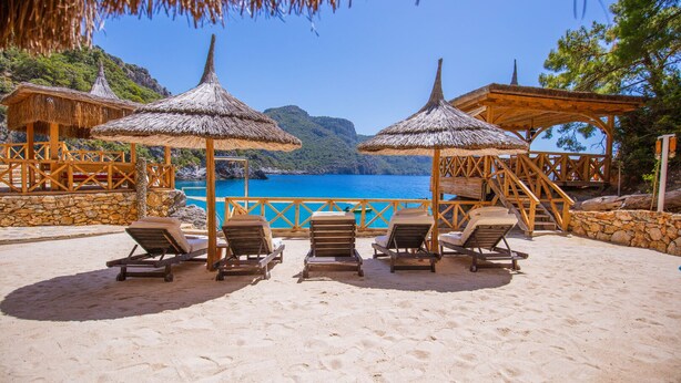 A beach with sun loungers and thatched umbrellas, overlooking a clear blue sea and green hills. - Private Island-Style Ultra Luxury Villa Estate (Fethiye)