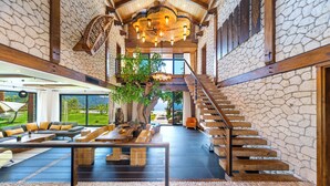 A spacious interior with a stone wall, a wooden staircase, and a large seating area with a tree centerpiece. - Private Island-Style Ultra Luxury Villa Estate (Fethiye)