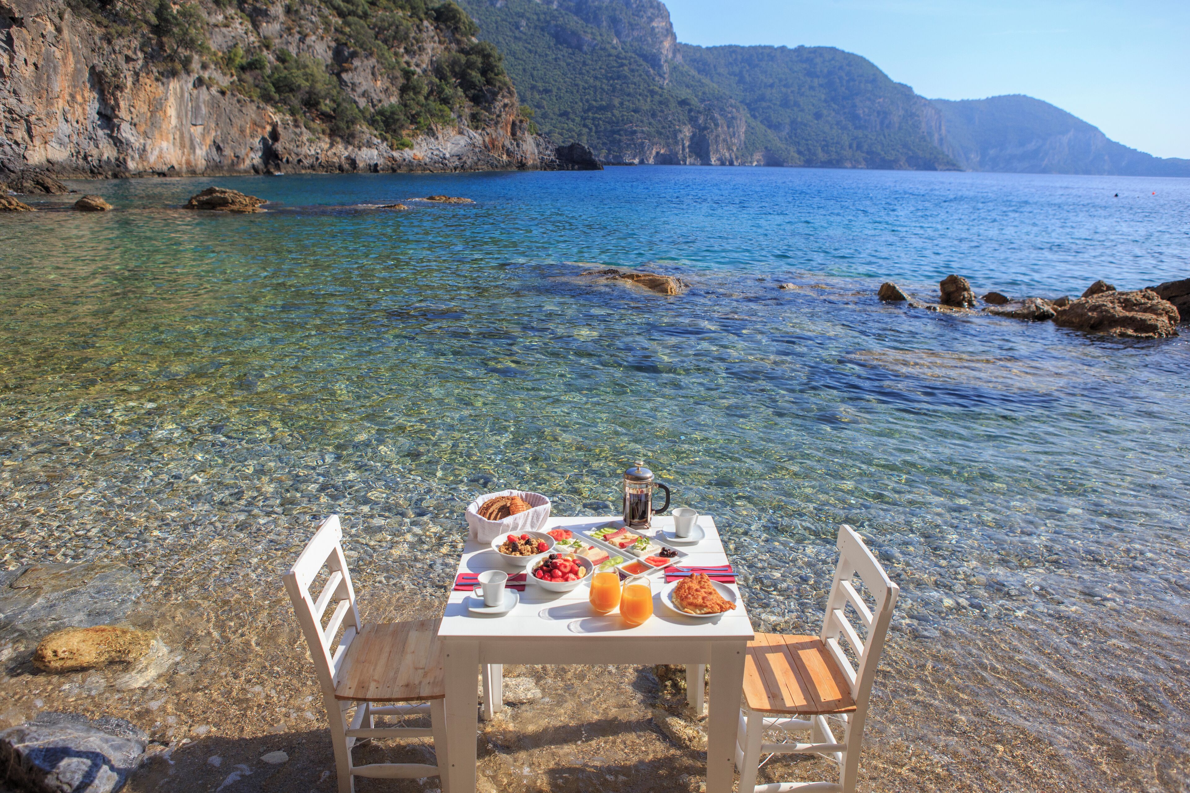 Una mesa montada en una orilla rocosa con agua transparente, con vistas a una costa montañosa.