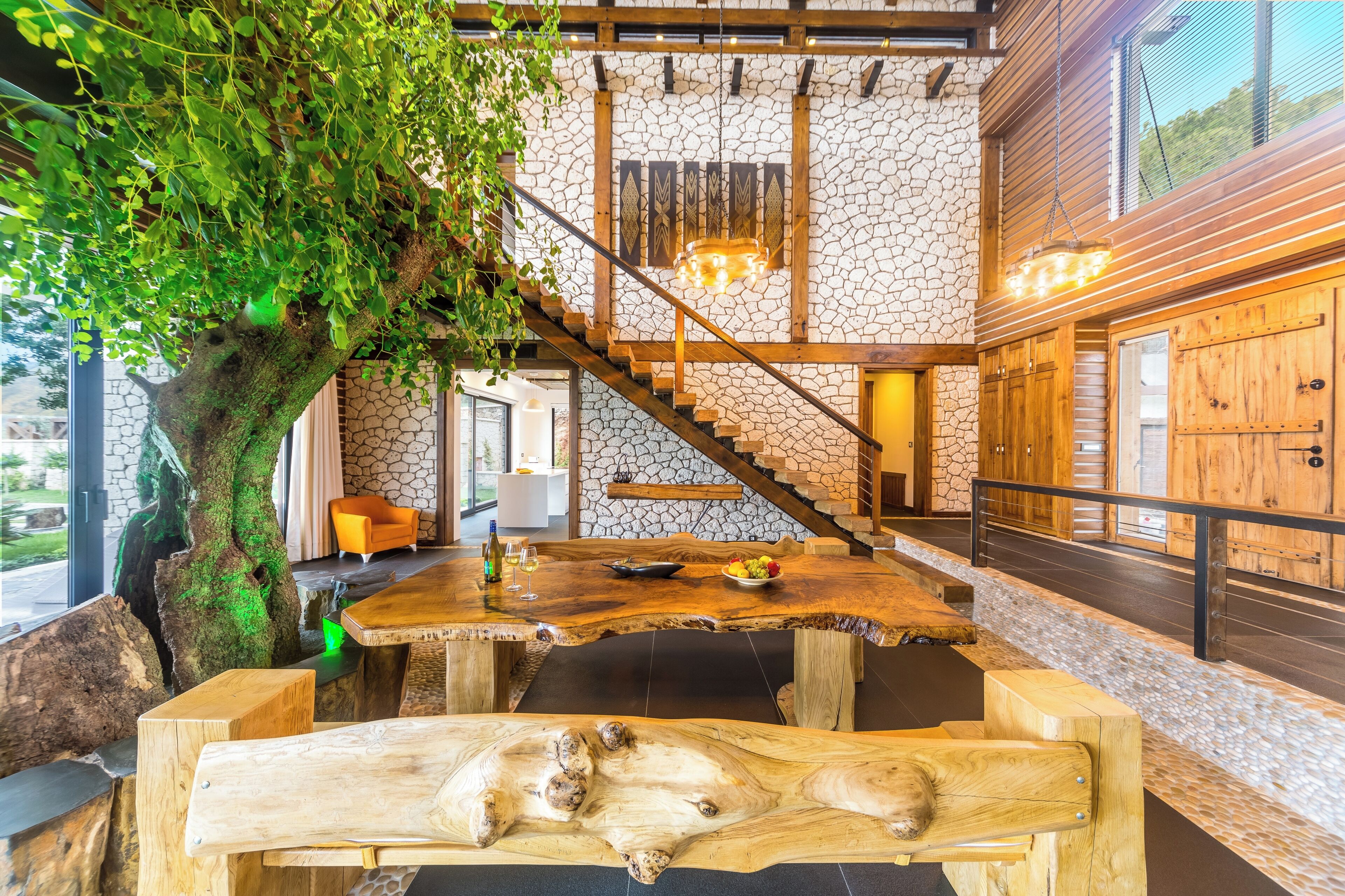 Un intérieur rustique avec une table à manger en bois, un grand arbre et un escalier menant à une mezzanine.