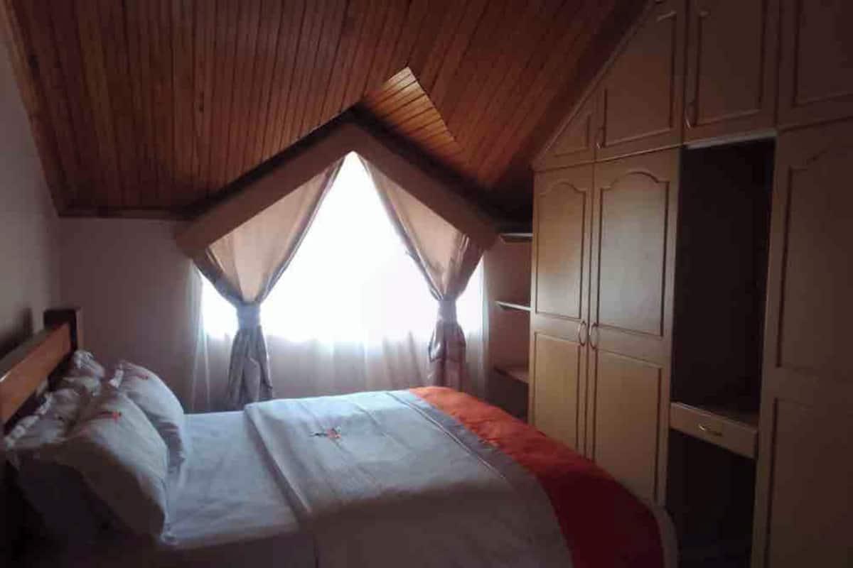 Une chambre avec un plafond en pente, un lit recouvert d’une housse de couette blanche et une armoire.