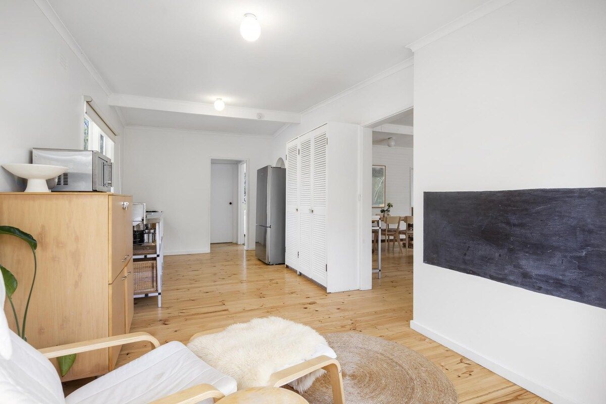 Une pièce moderne et bien éclairée, avec un lit, une armoire en bois, une chaise blanche et une grande œuvre d’art noire accrochée au mur.