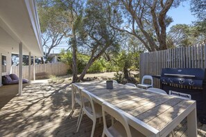Een terras buiten met een houten tafel en stoelen, een barbecue en een overdekte zithoek.