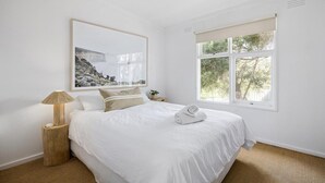 Een slaapkamer met een bed, een bedlampje, een raam en een ingelijste foto aan de muur.