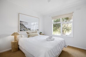 Een slaapkamer met een bed, een bedlampje, een raam en een ingelijste foto aan de muur.