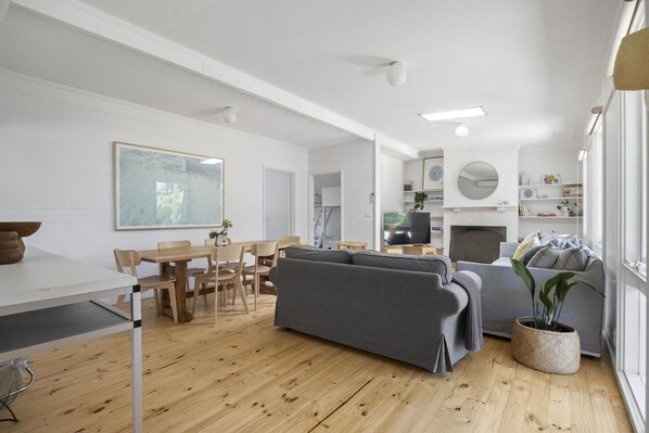 A modern living room with a sofa, dining table, and chairs, a fireplace, and a large window.