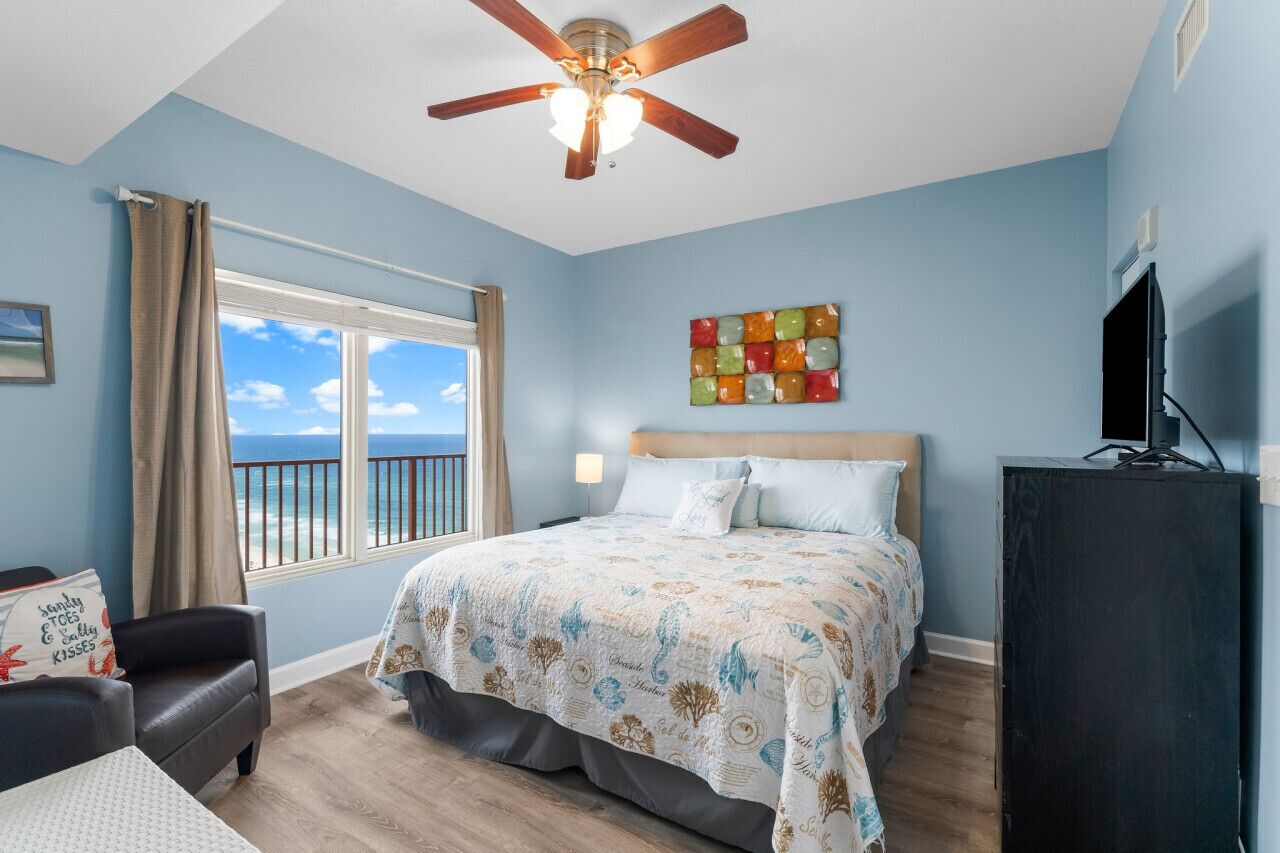 A bedroom with a bed, a ceiling fan, a window with a view, a TV, and a cabinet.