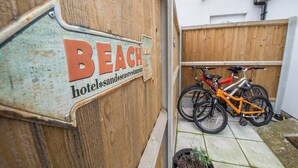 Ein hölzernes Schild mit der Aufschrift 'BEACH hotel sand sea restaurant' und zwei Fahrräder, die davor abgestellt sind.