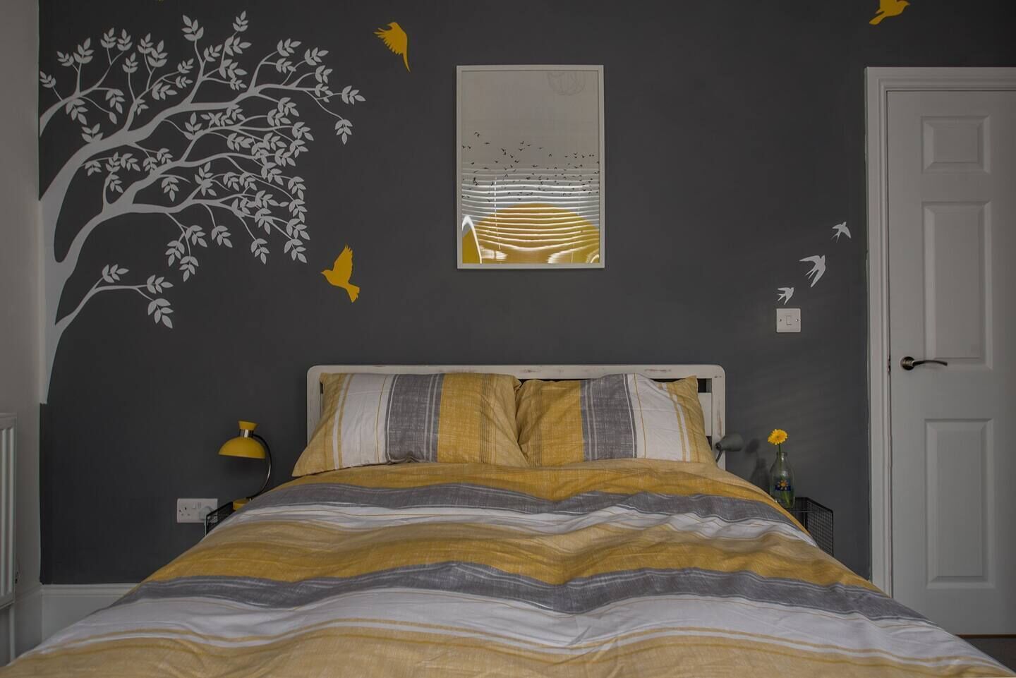 Un dormitorio con cama, un mural de un árbol y un cuadro enmarcado.