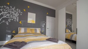 Ein Schlafzimmer mit einem Bett, einem Spiegel und einer Wand mit einer Wandmalerei von Baum und Vogel.