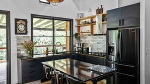 A modern kitchen with a large island, black cabinetry, stainless steel appliances, and a view of the outdoors. - Creekside Cottage pet friendly w pool (Perwillowen)