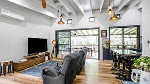 A modern living room with a flat-screen TV, leather recliners, a wooden entertainment unit, and a large window with a view of greenery. - Creekside Cottage pet friendly w pool (Perwillowen)