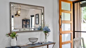 A room with a large mirror, a console table with decorative items, and a wooden door leading outside. - Creekside Cottage pet friendly w pool (Perwillowen)