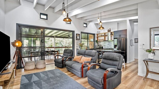 A spacious living room with a large window, a kitchen area, and a seating area with leather sofas. - Creekside Cottage pet friendly w pool (Perwillowen)