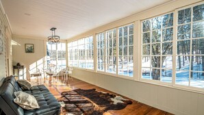 A spacious room with a large window, a leather sofa, and a wooden floor. - Huge Farmhouse Estate on South Pond with Extreme Privacy: Host Weddings (Buckfield)
