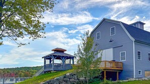 A large two-story house with a blue exterior, a wooden deck, and a stone staircase leading to a gazebo. - Huge Farmhouse Estate on South Pond with Extreme Privacy: Host Weddings (Buckfield)