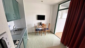 Una cucina funzionale con lavello e fornelli, una zona pranzo con tavolo e sedie, e un'ampia finestra con tende.