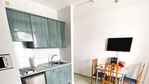 Una cucina compatta con mobili color acquamarina, lavastoviglie integrata e zona pranzo con tavolo e sedie.