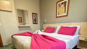 Una camera d'albergo con un letto, un comodino, uno specchio e un quadro appeso al muro.